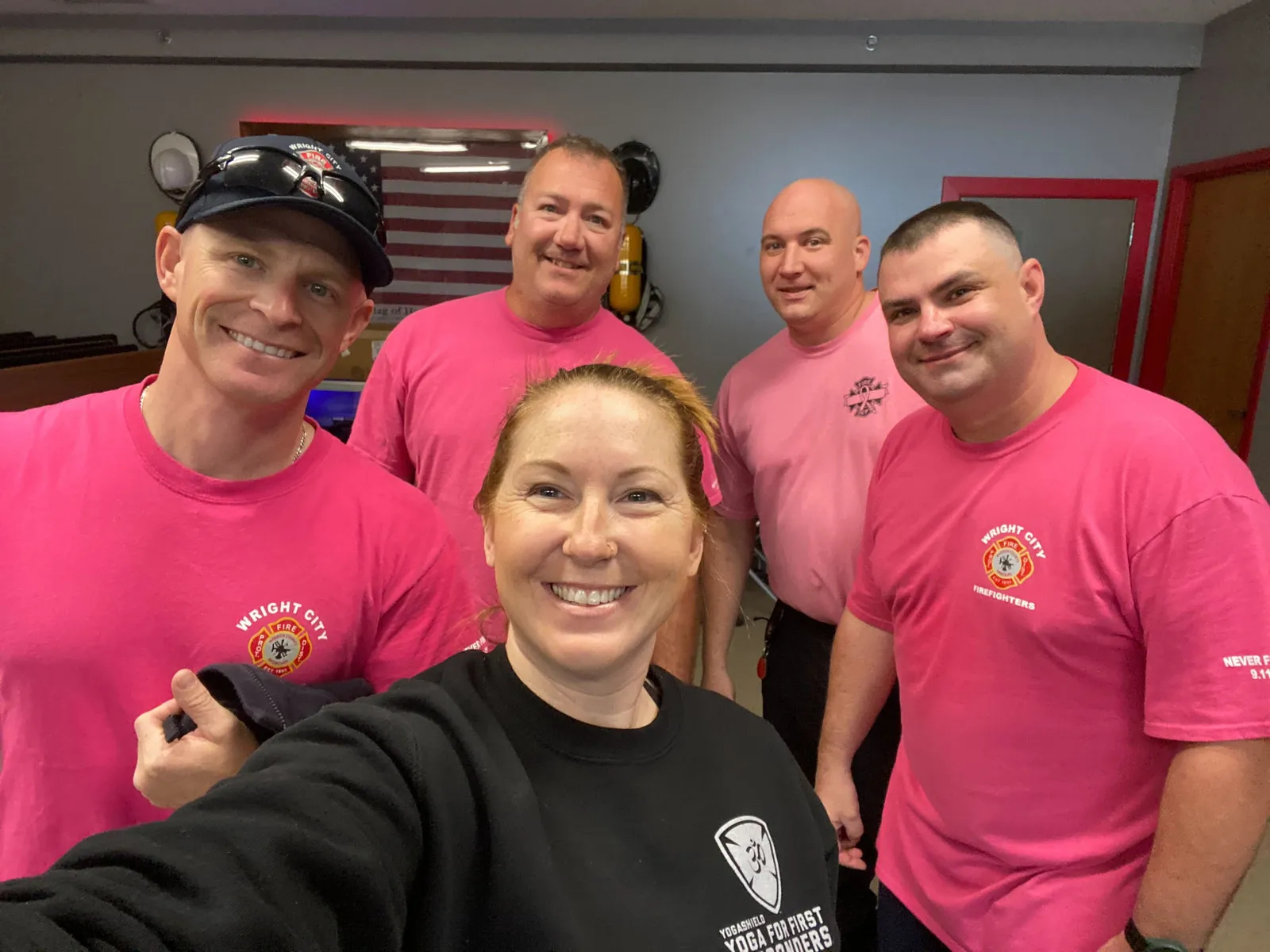 Woman surrounded by four firefighters wearing pink breast cancer awareness shirts