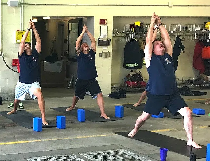 3 Firefighters on yoga mats practicing Warrior 1